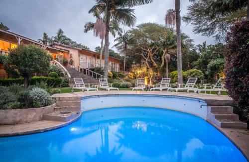 a swimming pool with chairs and palm trees at Petite Provence B&B in Ballito