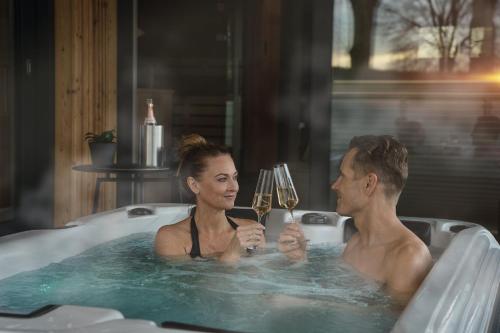a man and woman in a bathtub with glasses of wine at VÜ Terrassen-Chalets in Münchberg