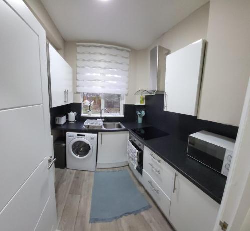 cocina con armarios blancos, lavadora y secadora en Warm cosy family home en East Tilbury