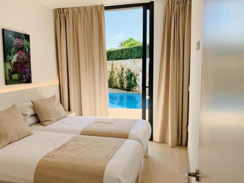 two beds in a hotel room with a large window at Villa SONIA in Cala en Blanes