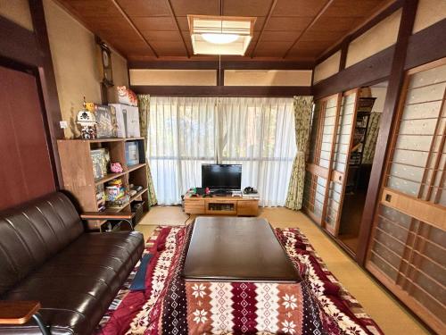 sala de estar con sofá de cuero y TV en ゲストハウスでたらめ荘, en Yamakami