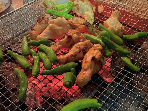 una parrilla con pollo y pimientos verdes. en ゲストハウスでたらめ荘 en Yamakami