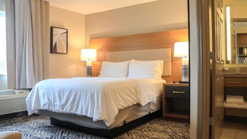 a hotel room with a bed with white sheets and pillows at Candlewood Suites - Peoria at Grand Prairie by IHG in Peoria