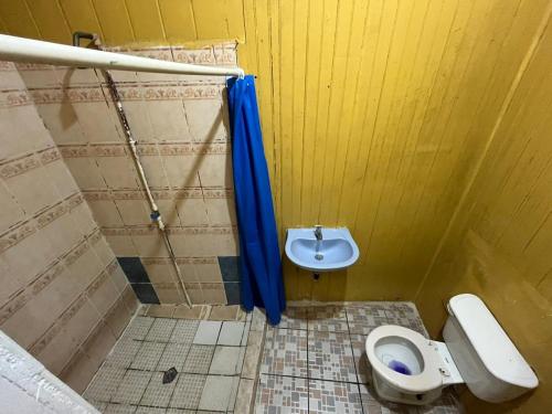 a bathroom with a toilet and a blue shower curtain at Hotel Gusto Bueno in Coxen Hole