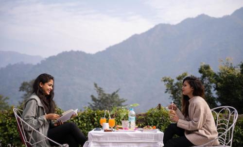 deux femmes assises à une table en lisant des livres dans l'établissement Swiss Cottage and Spa by Salvus, à Rishikesh