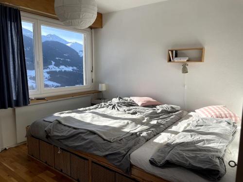 an unmade bed in a bedroom with a window at Casa Splendusa - sonnige Wohnung in Brigels in Breil/Brigels