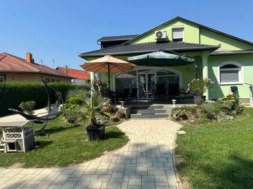 a green house with an umbrella and a patio at Rena Vendégház in Nagykanizsa