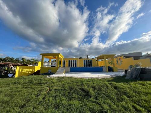una casa amarilla en un campo con un cielo nublado en Casa De Sol Family Home Near Rincon & Beach en Aguada