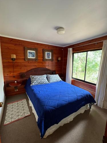 ein Schlafzimmer mit einem Bett mit blauer Decke und einem Fenster in der Unterkunft Cabaña Pingüeral (Derecho a piscina verano) in Dichato