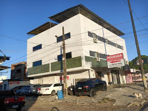 un bâtiment blanc avec des voitures garées devant lui dans l'établissement Pousada caminho das praias jp, à João Pessoa