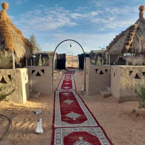 a group of houses with a red rug on the ground at RestCamp ErgChebbi in Merzouga
