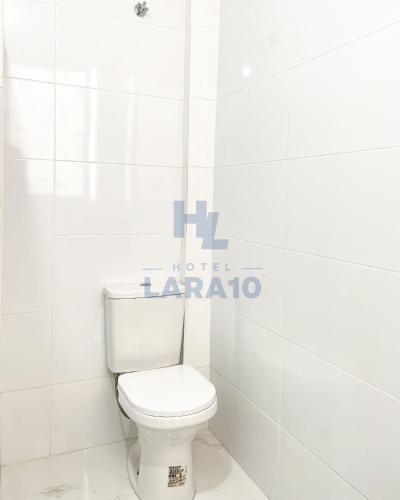 a white toilet in a bathroom with a sign on the wall at Hotel Lara 10 Curitiba in Curitiba
