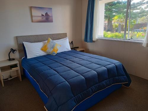 - un lit bleu dans une chambre avec fenêtre dans l'établissement Beaches Motel, à Waihi Beach