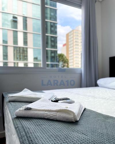 a bed with a towel on it in front of a window at Hotel Lara 10 Curitiba in Curitiba