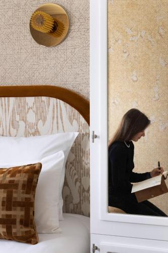 a woman sitting on a bed reading a book at Hotel des Carmes by Malone in Paris