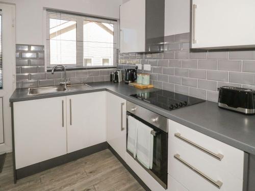 a kitchen with white cabinets and a sink at Bay View Bungalow Benllech, 5 Min Walk from Beach in Benllech