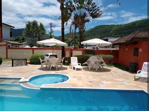 a swimming pool with chairs and umbrellas next to a house at Flat charmoso na praia de Juquehy in São Sebastião