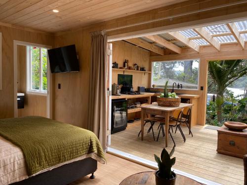 a bedroom with a bed and a desk and a kitchen at The Bay Cottage - Located Directly Across the Road from 2 Swimming Beaches in Great Barrier Island