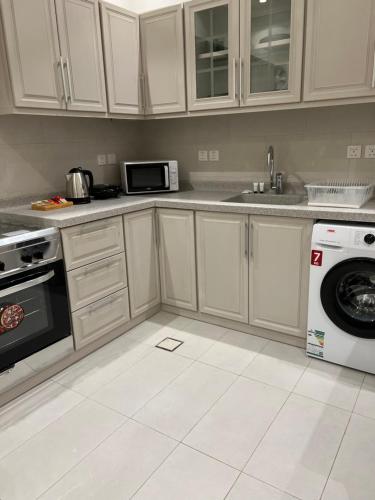 eine Küche mit weißen Schränken, einer Waschmaschine und einem Trockner in der Unterkunft ALMALQA HAVEN - الملقا - الرياض in Riad