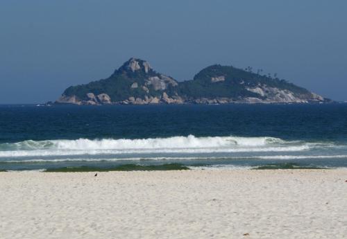 a beach with a mountain in the ocean with waves at Tropical Barra Hotel in Rio de Janeiro
