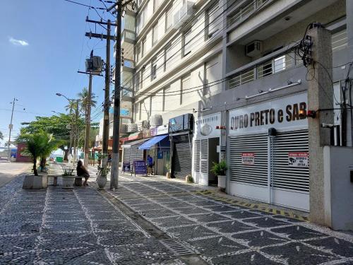 une personne assise sur un trottoir à côté d'un bâtiment dans l'établissement Ótima Kitnet pé na areia na praia de Pitangueiras c/ vista para o mar., à Guarujá