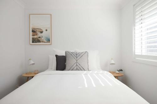 een wit bed in een witte slaapkamer met 2 lampen bij No 2 Luana in Nelson Bay
