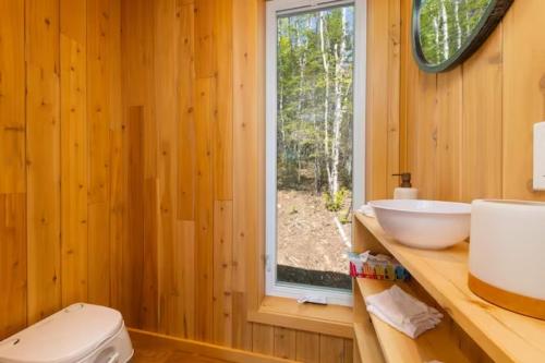 baño con aseo y lavabo y ventana en Tanières MicroChalets Charlevoix en Baie-Saint-Paul