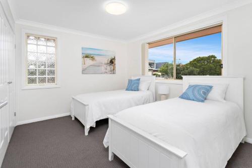 two beds in a white room with a window at Sea La Vie in Shellharbour