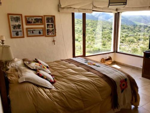 ein Schlafzimmer mit einem Bett mit Kissen und einem großen Fenster in der Unterkunft La Escondida Tafi del Valle in Tafí del Valle