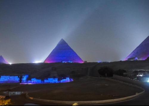 una vista de las pirámides por la noche con luces púrpuras en Pyramids hotel, en El Cairo