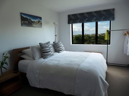 um quarto com uma cama branca com almofadas e uma janela em Te Rukutai em Auckland