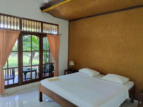 a bedroom with a bed and a large window at Bayumantra Bungalows in Lovina
