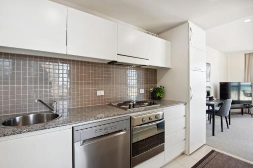 a kitchen with white cabinets and a sink at Belle Escapes - Beachfront Balcony Glenelg in Glenelg