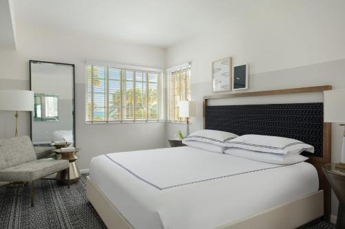 a white bedroom with a large bed and a chair at Kimpton Surfcomber Hotel by IHG in Miami Beach