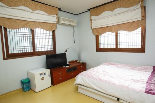 a bedroom with a bed and a tv and windows at Jun Motel in Jeju