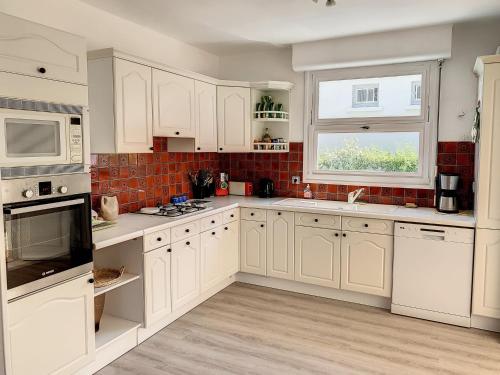 une cuisine blanche avec des armoires blanches et une fenêtre dans l'établissement Maison de vacances à 350m de la plage avec jardin, véranda et Wi-Fi gratuit - FR-1-361-525, à Saint-Pair-sur-Mer