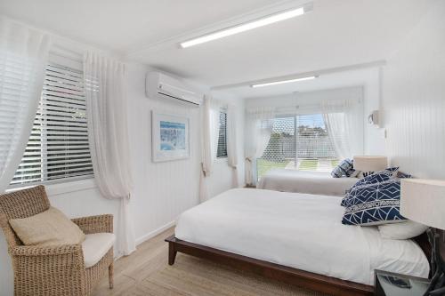een witte slaapkamer met een bed en een stoel bij Oceanfront Beach House On Marine Parade in Kingscliff