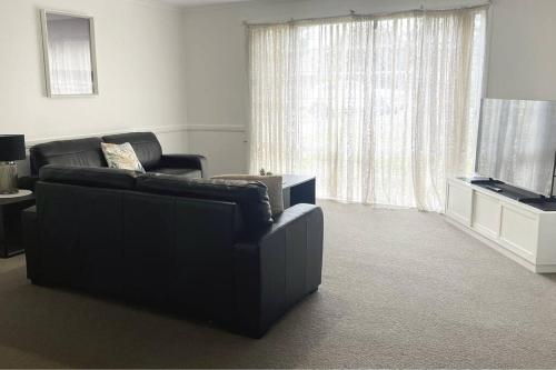 a living room with a black couch and a television at Suburban Bliss - Elegant Villa 1 in Wagga Wagga