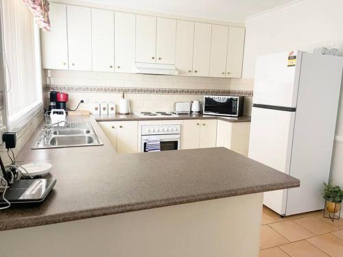 a kitchen with white cabinets and a white refrigerator at Suburban Bliss - Elegant Villa 2 in Wagga Wagga