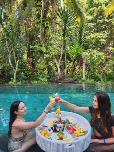 two women sitting around a table with food in a pool at Luxury 3BR Infinity Jungle View Aashaya Villa Ubud in Ubud