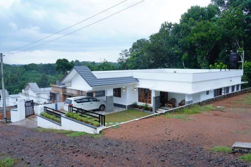 ein weißes Haus mit einem Auto in der Einfahrt in der Unterkunft Woodland Escape Villas by Lexstays in Ettumānūr