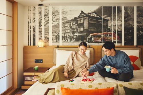 箱根町にあるホテルインディゴ箱根強羅の男女がベッドに座って食べ物を食べる