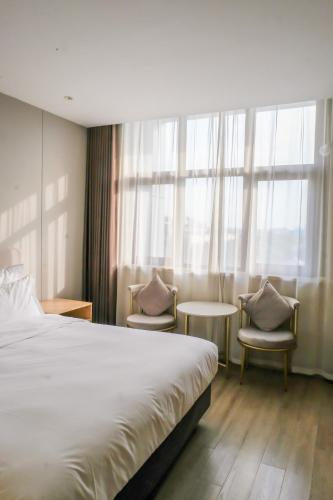 a hotel room with a bed and two chairs and a window at Shanghai JOYFUL YARD Hotel-Free shuttle bus to Pudong Airport and Disneyland in Shanghai