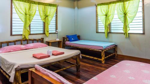 a room with two beds and a bench and windows at High Chaparral Cottages in El Nido