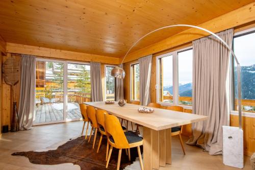 une salle à manger avec une table, des chaises et des fenêtres dans l'établissement Chalet Gemme - Magnifique chalet piscine sauna, à Saint-Étienne-de-Tinée