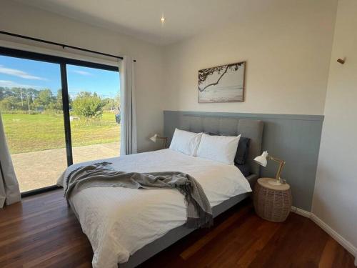um quarto com uma cama e uma grande janela em The Ranch - Coastal Farmhouse midway to Newcastle Airport and Beaches em Salt Ash
