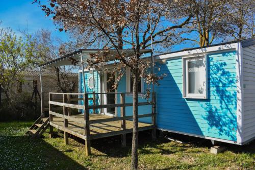 una casita azul con un porche y un árbol en CAMPING LE NAVARRE *** en Vias