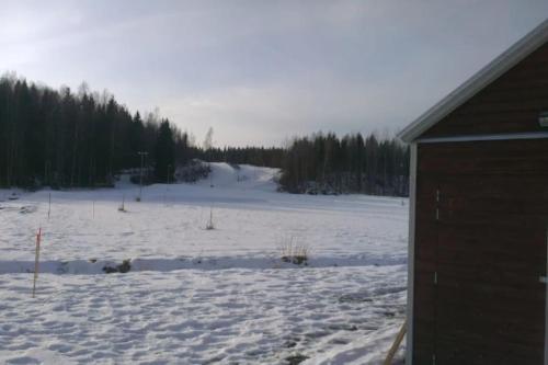 a snow covered field with trees and a building at Stuga Fyra Säsonger - Fishing - Skiing - Hottub in Filipstad