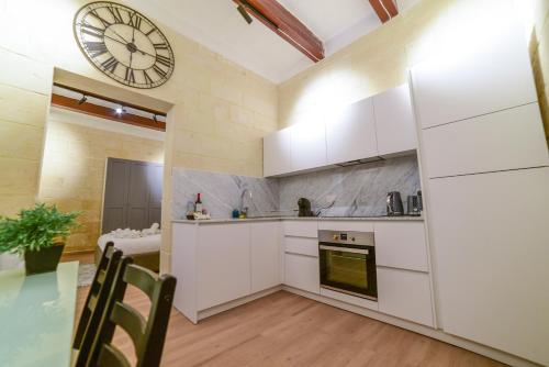 a kitchen with white cabinets and a clock on the wall at Valletta Collection - Felix Apartments in Valletta