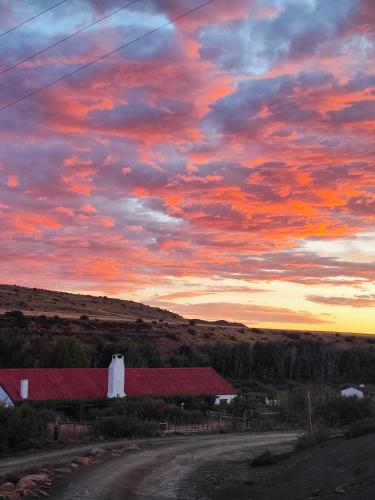 a sunset over a road with a red roof at Ganora Guest Farm, Camping and Excursions in Nieu-Bethesda